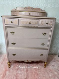 a white dresser with gold handles and drawers on top of pink furnishing in front of a blue wall