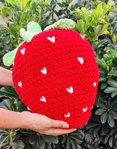 a hand holding a red knitted strawberry pillow