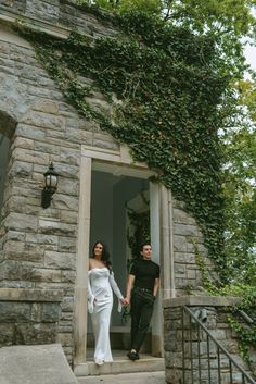 a man and woman walking out of a stone building with ivy growing up the side