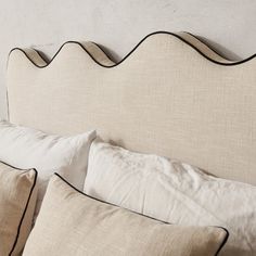 an upholstered headboard with black piping and white linens on it