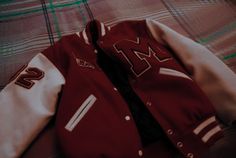 a maroon and white jacket laying on top of a plaid bed spread next to a pillow