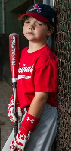 a young boy holding a baseball bat leaning against a fence