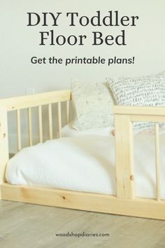 a wooden bed with white sheets and pillows next to a wall that says diy toddler floor bed get the printable plans