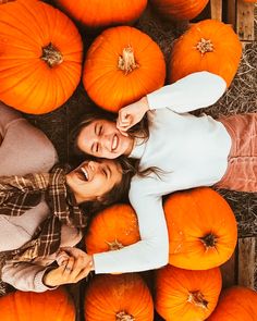 two women standing next to each other surrounded by pumpkins