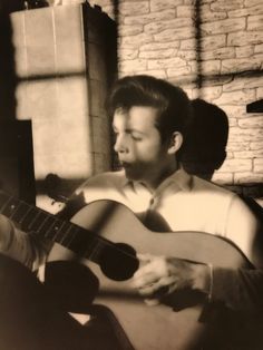 a young man playing an acoustic guitar in front of a brick wall