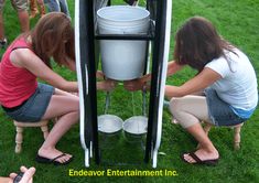 three women are filling buckets into an outdoor water dispenser in the grass