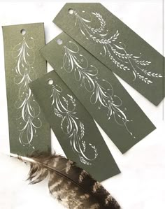 four tags with white designs on them and a feather