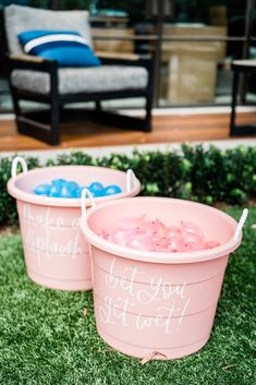 two pink buckets filled with water sitting on the grass