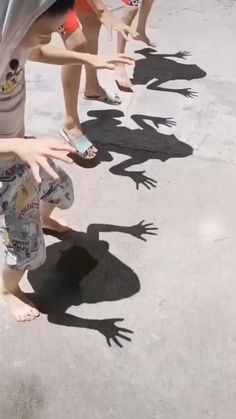 several children are standing in a line with their shadows on the ground and one child is reaching for something