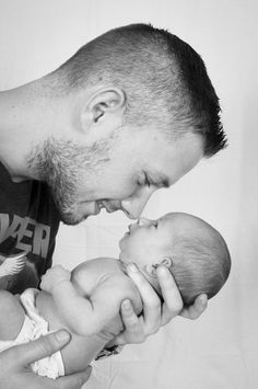 a man holding a baby and kissing it's face with his mouth open in black and white