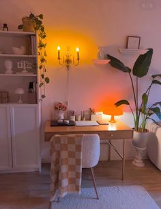 a room with a desk, chair and potted plant on it in front of a yellow light