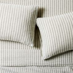 two pillows on top of a bed with white and gray striped sheets in the background