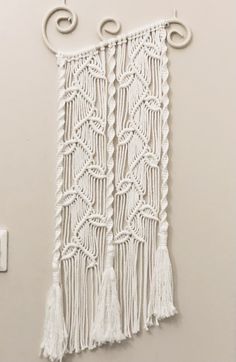 a white wall hanging on the side of a wall with two hooks and some tassels attached to it