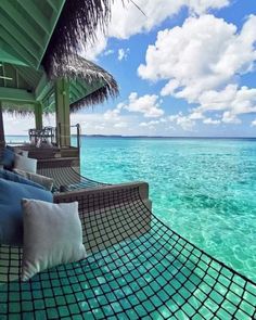 a hammock hanging over the ocean with blue skies and clouds in the background