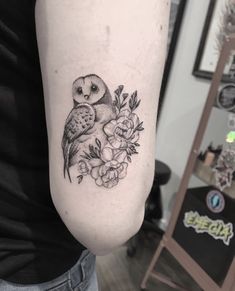 an owl and flowers tattoo on the right arm, which is also in black and white