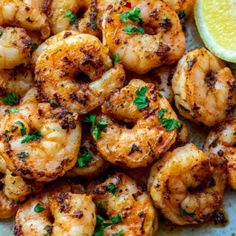 grilled shrimp with lemon wedges and parsley on a white plate next to a slice of lime