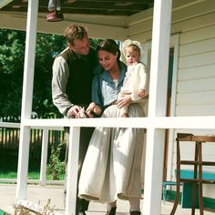 a man and woman are standing on the porch with a baby in their arms,