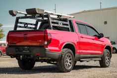 a red pick up truck parked in front of a building with a surfboard rack on the back