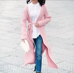 a woman wearing jeans and a pink cardigan is walking down the street with her hand in her pocket