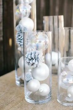 three clear vases filled with white balls and snowflakes on a wooden table