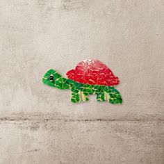 a red and green turtle sitting on top of a cement wall