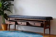 a wooden bench with drawers underneath it next to a potted plant on the floor