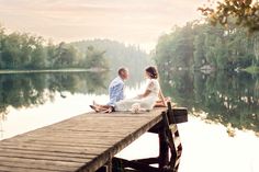 a man and woman sitting on a dock by the water