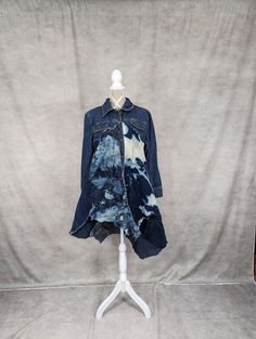 a blue jean jacket on a white mannequin stand with a gray backdrop behind it