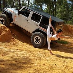 a woman doing yoga in front of a jeep on a dirt hill with trees in the background