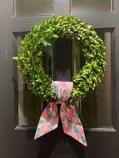 a green wreath with pink and blue flowers is hanging on the front door, next to a pair of scissors