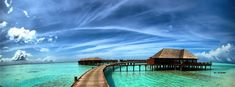 a pier leading into the ocean next to a wooden house with thatched roof on it