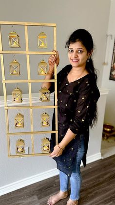 a woman standing in front of a wall holding up a piece of art that is made out of metal