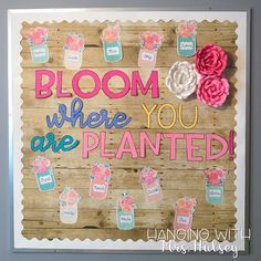 a sign that says bloom where you are planted hanging with pink flowers on a gray wall