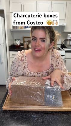 a woman sitting at a kitchen counter with a box in front of her and the caption'characterie boxes from costco '