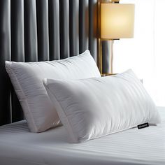 two white pillows sitting on top of a bed next to a night stand with a lamp