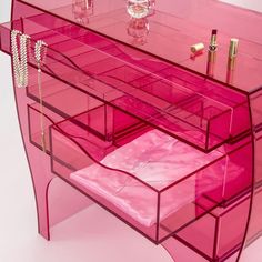 a pink vanity with lots of drawers and lipstick on the top shelf, in front of a white wall