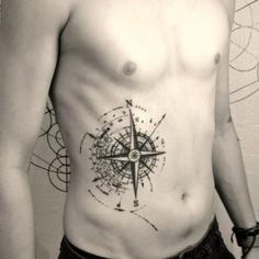 a man with a compass tattoo on his chest is standing in front of a wall