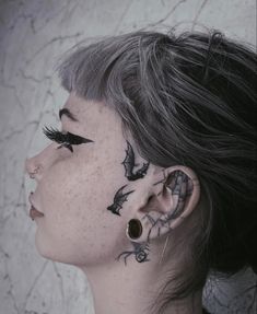 a woman with black tattoos on her face and behind her ear is looking at the sky