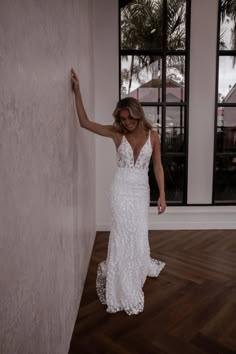 a woman in a white dress leaning against a wall with her hand on the wall