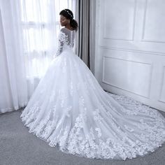 a woman in a white wedding dress is standing near a window with sheer drapes