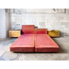 a red couch sitting on top of a cement floor next to two yellow chests and a white tiled wall