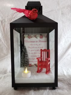 a small lantern with a red rocking chair on it and a lit candle in the middle