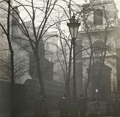 an old black and white photo of a street light in the middle of a city