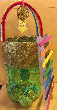 a green bucket filled with lots of coins next to a wooden stick and rainbow sticks