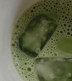 two ice cubes sitting in a white bowl filled with green liquid and some bubbles