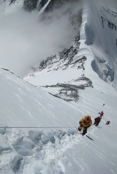 several people climbing up the side of a snow covered mountain