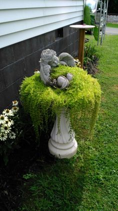 two stuffed animals sitting on top of a planter covered in green moss next to a house