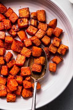 a white plate topped with cooked sweet potatoes and a spoon next to it on a table