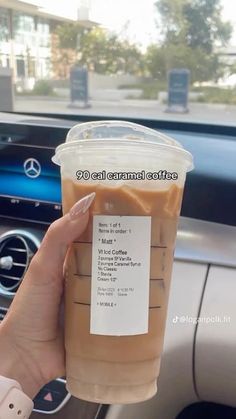 a woman holding up a cup of coffee in her car