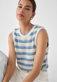 a woman is sitting down wearing a blue and white knitted top with open shoulders